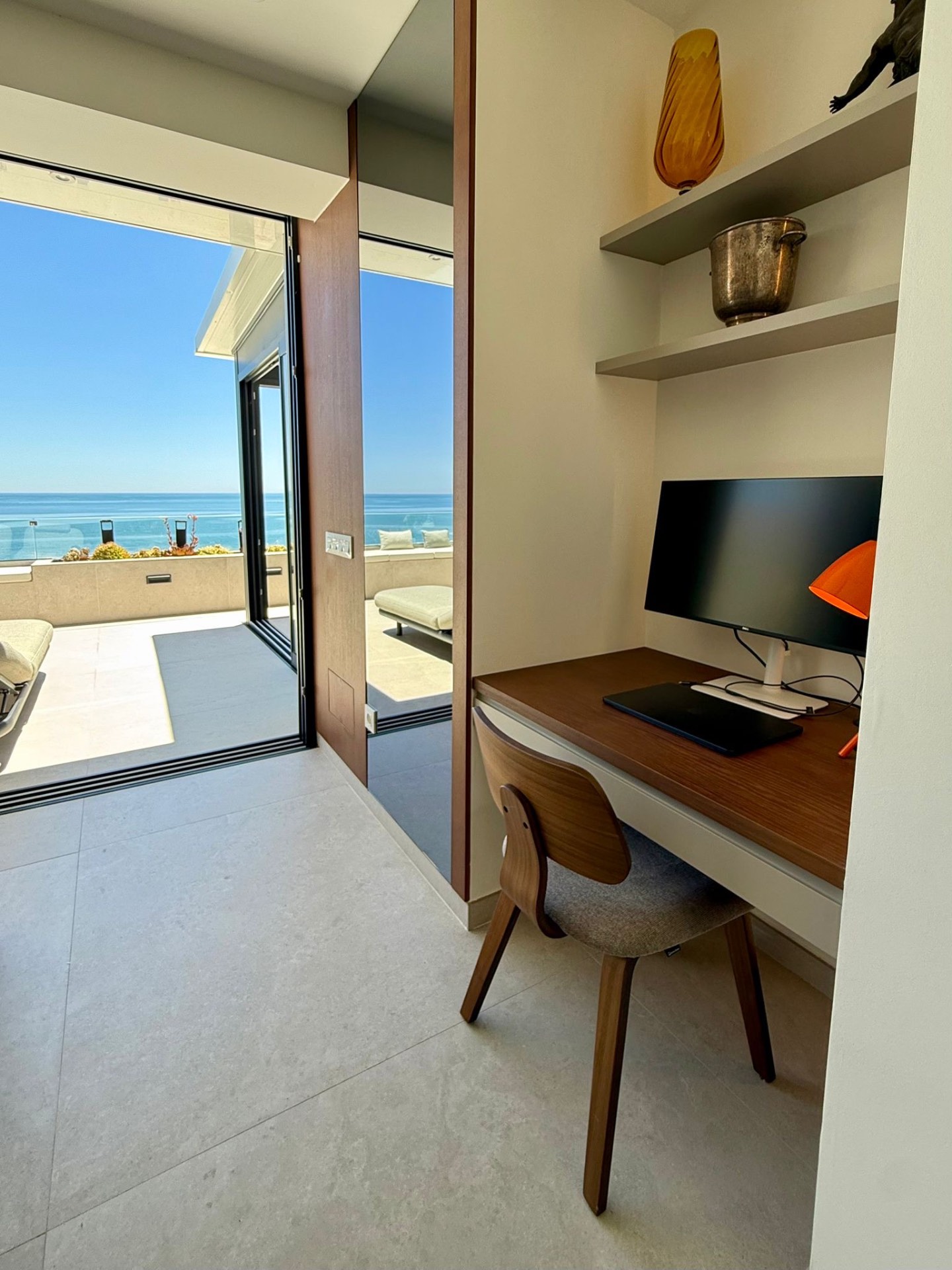 A desk with its own screen, the sea through the open terrace doors